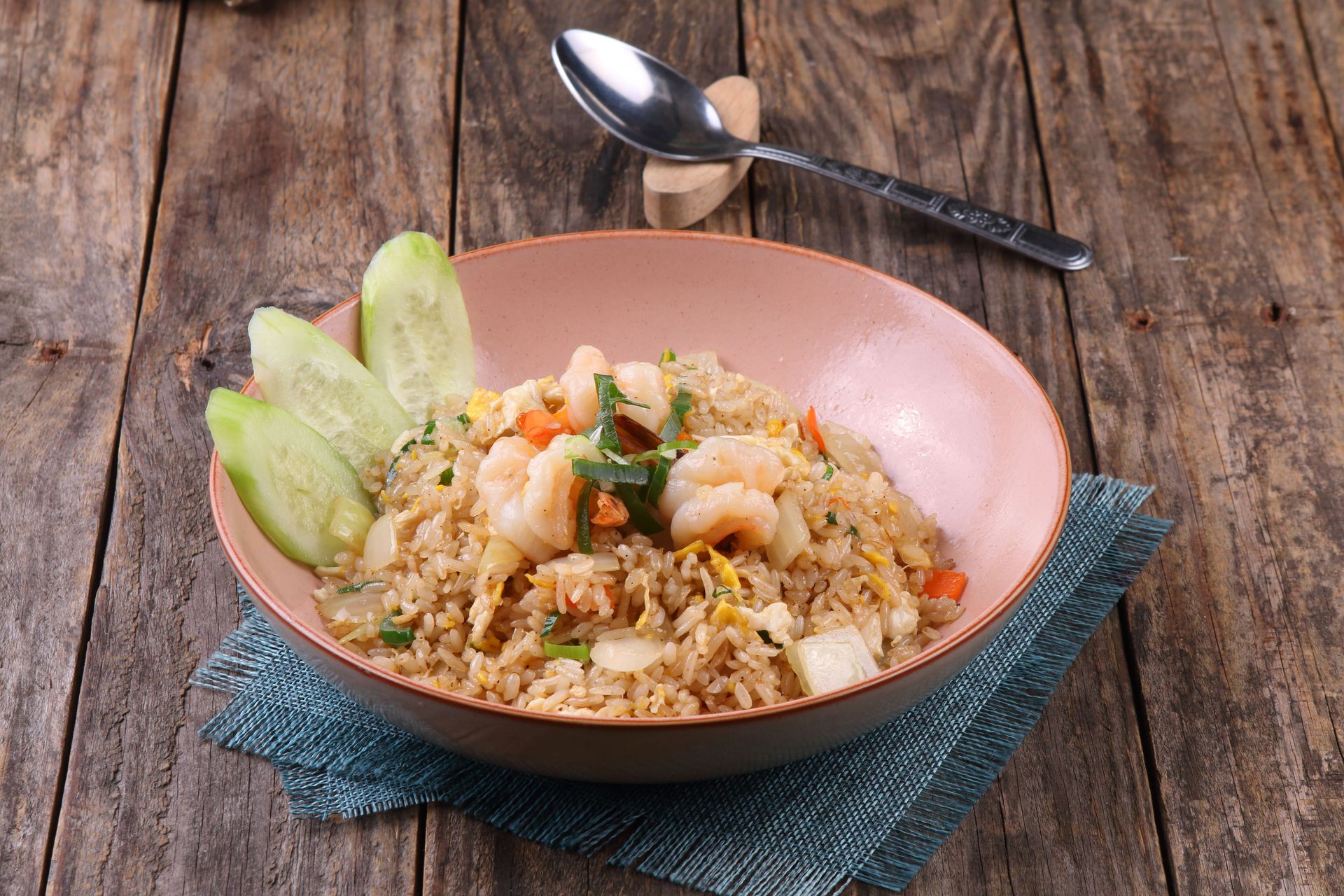 Appetizing shrimp fried rice with cucumbers in a bowl on wooden table.